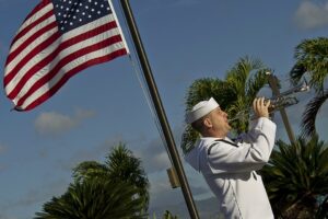 Trompettiste de la marine américaine en uniforme blanc jouant de la trompette à côté d'un drapeau, sous les palmiers